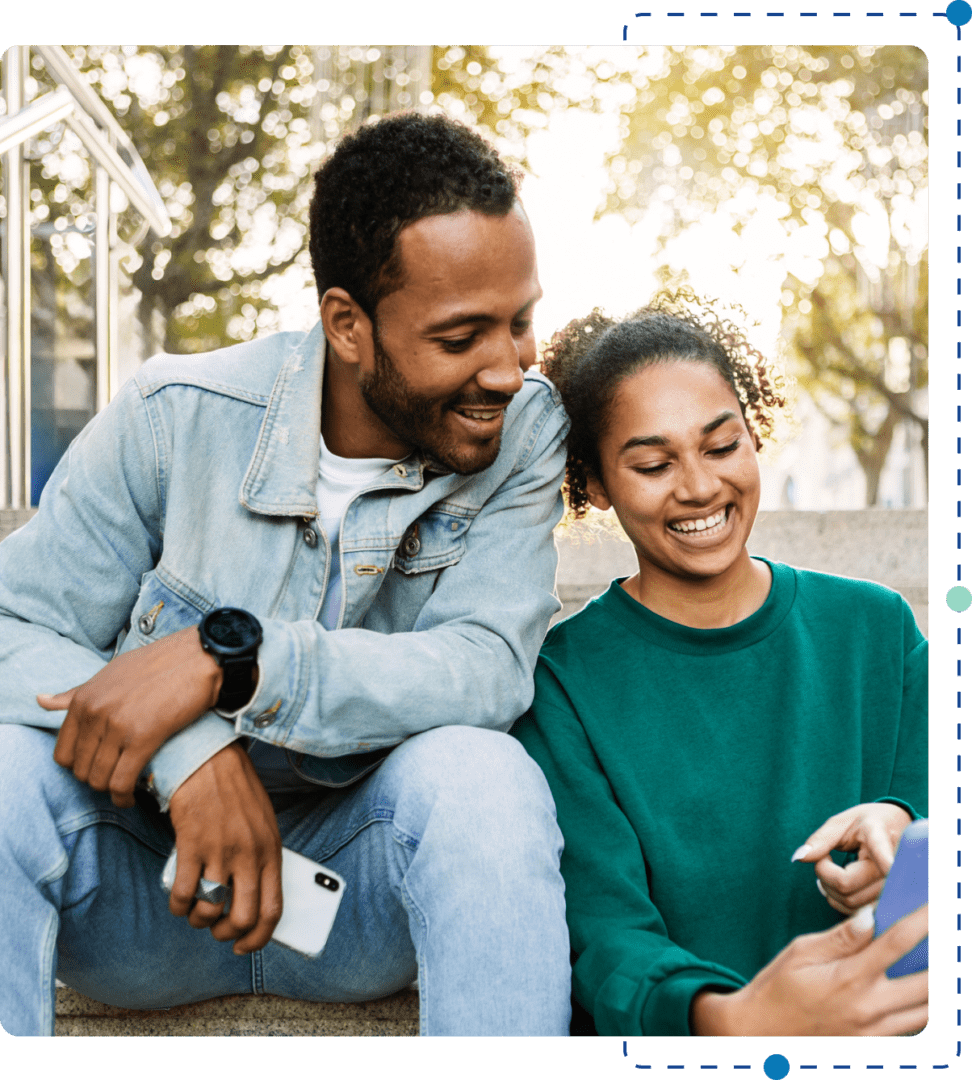 A man and woman sitting on the ground looking at a phone.